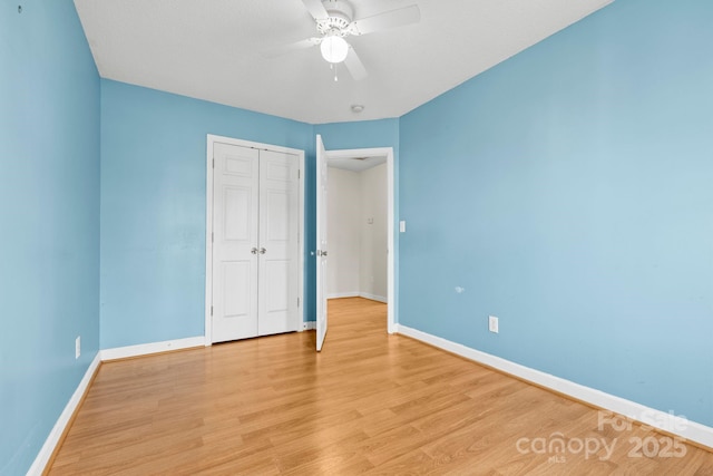 unfurnished bedroom featuring baseboards, ceiling fan, a closet, and light wood-style floors