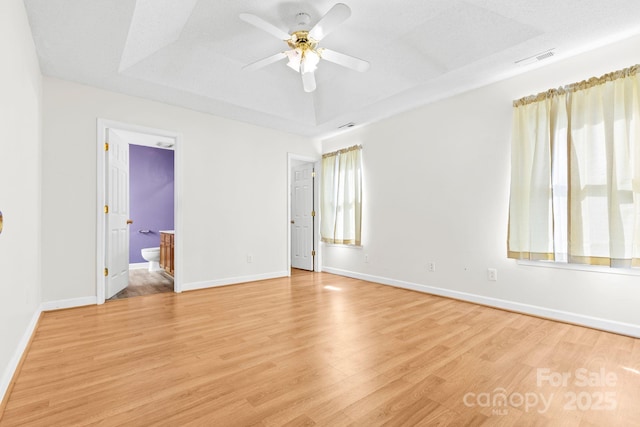 spare room with light wood-style floors, visible vents, a tray ceiling, and baseboards