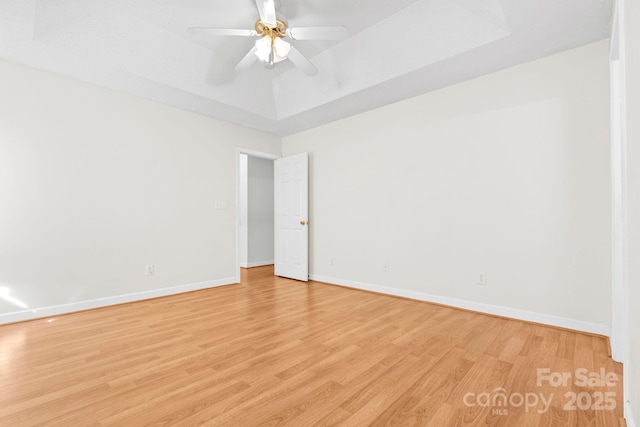 empty room with light wood finished floors, ceiling fan, baseboards, and a tray ceiling