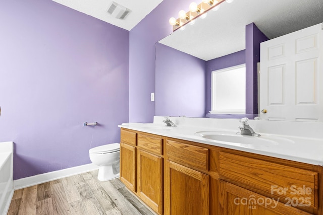 bathroom with toilet, wood finished floors, a sink, and visible vents