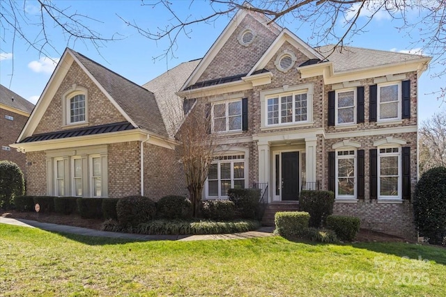 view of front of home featuring a front lawn, a standing seam roof, a shingled roof, metal roof, and brick siding