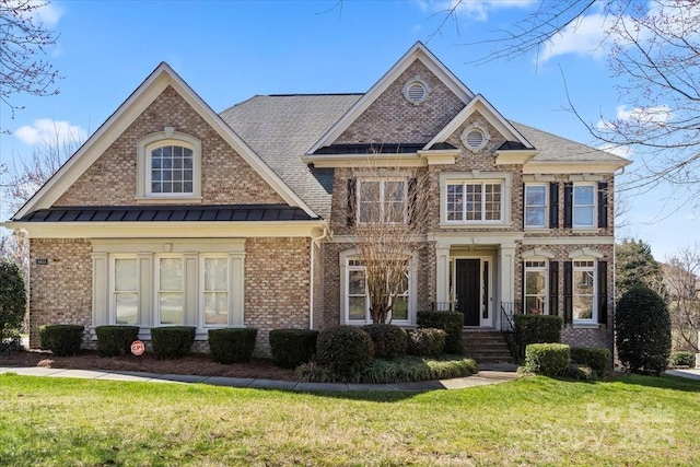 view of front of property featuring brick siding, a front lawn, a standing seam roof, and metal roof