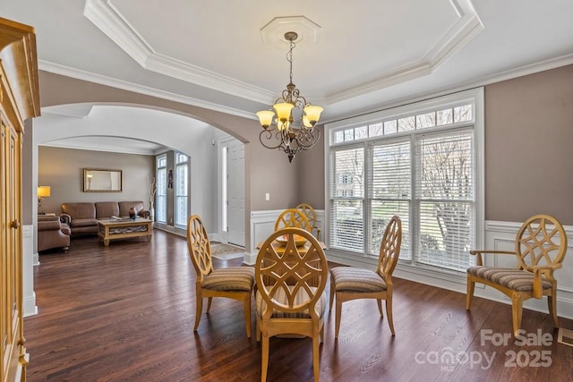 dining room featuring a wainscoted wall, a notable chandelier, arched walkways, plenty of natural light, and a raised ceiling