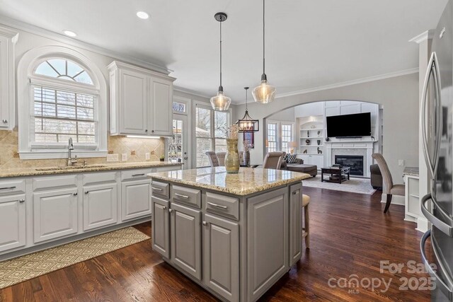 kitchen featuring dark wood-style flooring, gray cabinets, freestanding refrigerator, a sink, and a glass covered fireplace