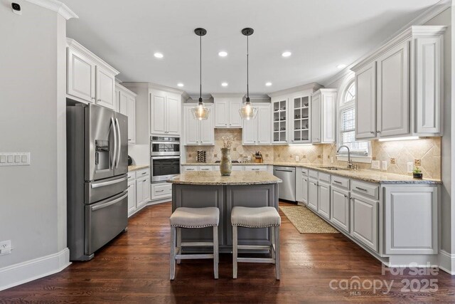 kitchen featuring dark wood-style floors, a sink, appliances with stainless steel finishes, white cabinetry, and a center island