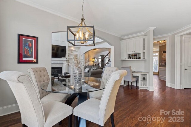 dining space featuring crown molding, a notable chandelier, stairs, dark wood-style floors, and a glass covered fireplace