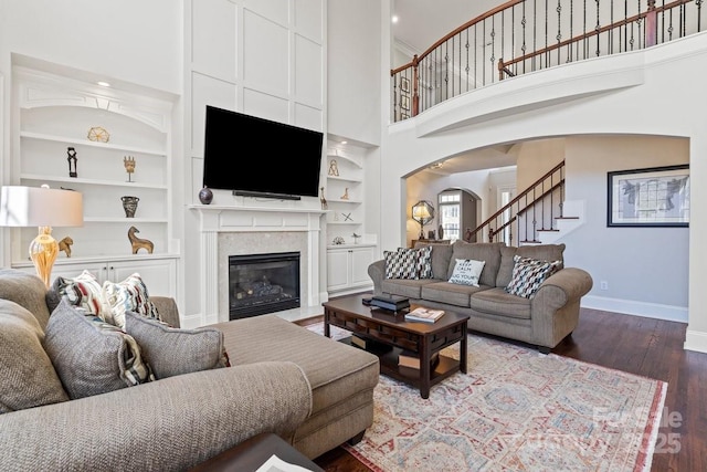 living room featuring built in shelves, wood finished floors, arched walkways, a fireplace, and baseboards