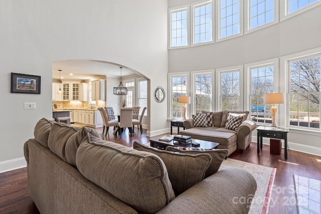 living room with arched walkways, a towering ceiling, baseboards, and dark wood-style flooring