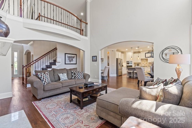 living area featuring baseboards, dark wood finished floors, a high ceiling, arched walkways, and stairs