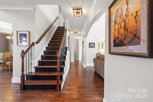 staircase with wood finished floors, baseboards, arched walkways, crown molding, and a notable chandelier