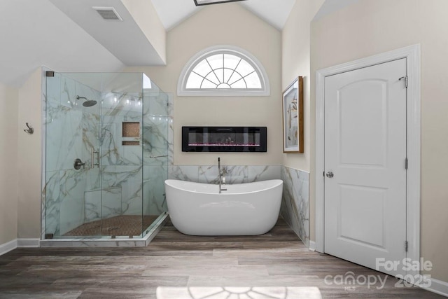 full bathroom featuring visible vents, wood finished floors, a marble finish shower, lofted ceiling, and a freestanding bath