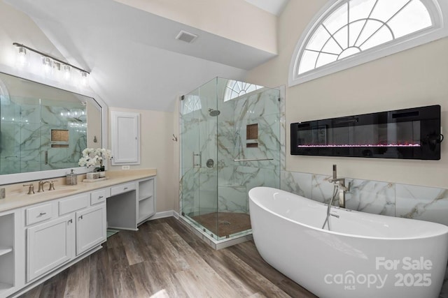 bathroom featuring wood finished floors, visible vents, a marble finish shower, lofted ceiling, and a glass covered fireplace