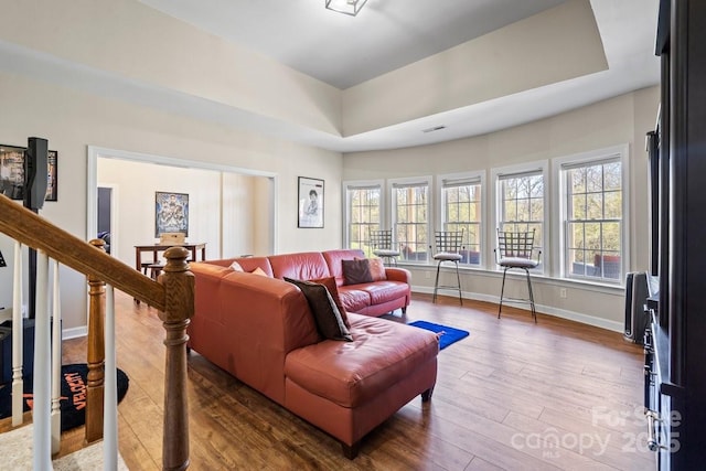 living room with visible vents, a tray ceiling, wood finished floors, stairway, and baseboards