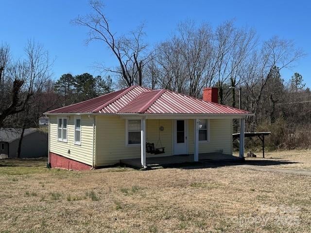 view of front of property with covered porch, metal roof, a front lawn, and a chimney