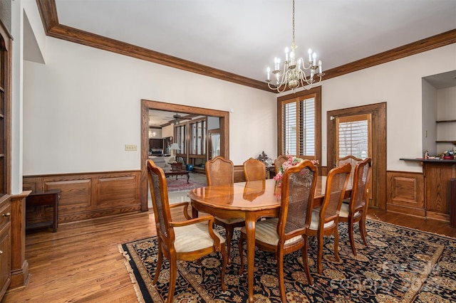 dining room featuring wainscoting, ceiling fan with notable chandelier, light wood-style flooring, and ornamental molding