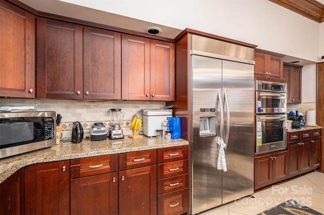 kitchen with light tile patterned flooring, backsplash, appliances with stainless steel finishes, and light stone countertops