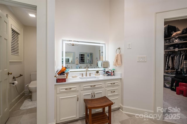 bathroom featuring toilet, vanity, tile patterned flooring, baseboards, and a spacious closet