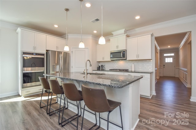 kitchen featuring a center island with sink, visible vents, a kitchen breakfast bar, stainless steel appliances, and a sink