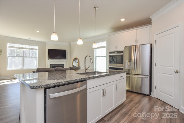 kitchen featuring appliances with stainless steel finishes, ornamental molding, dark stone countertops, a fireplace, and a sink