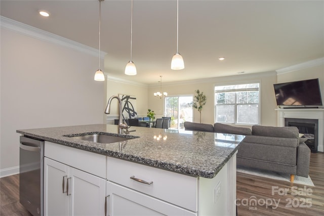 kitchen featuring dark stone counters, dishwasher, ornamental molding, a kitchen island with sink, and a sink