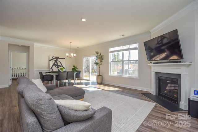 living room featuring a chandelier, dark wood-style flooring, baseboards, ornamental molding, and a glass covered fireplace