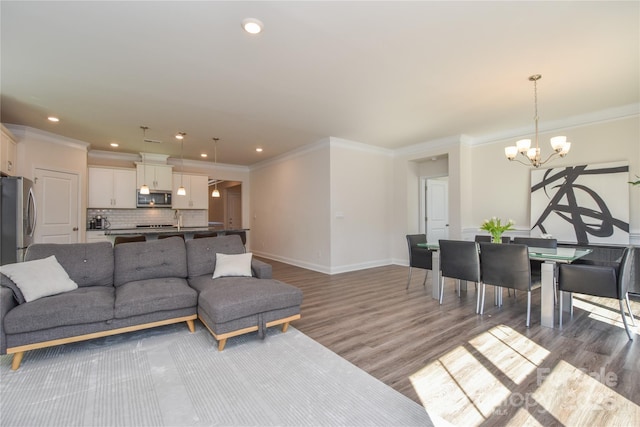 living area featuring ornamental molding, baseboards, a notable chandelier, and light wood finished floors