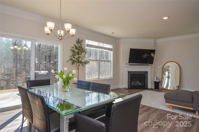 dining space featuring a notable chandelier, a fireplace with flush hearth, wood finished floors, baseboards, and ornamental molding