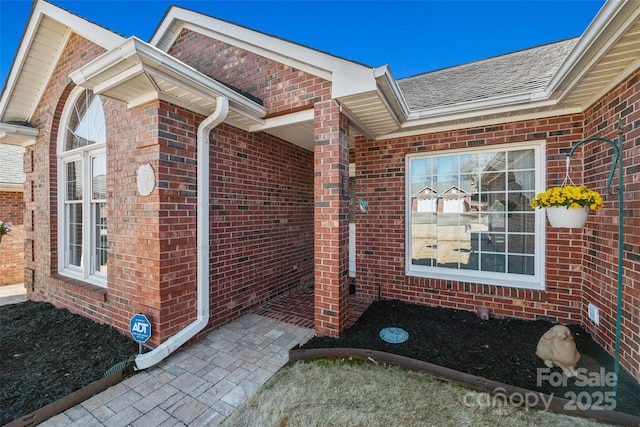 view of exterior entry with brick siding and roof with shingles