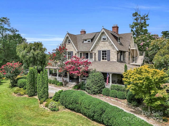 shingle-style home featuring stairway, a front yard, a porch, and a chimney