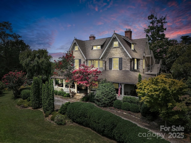 view of front of home featuring stairway, a yard, covered porch, a chimney, and stone siding