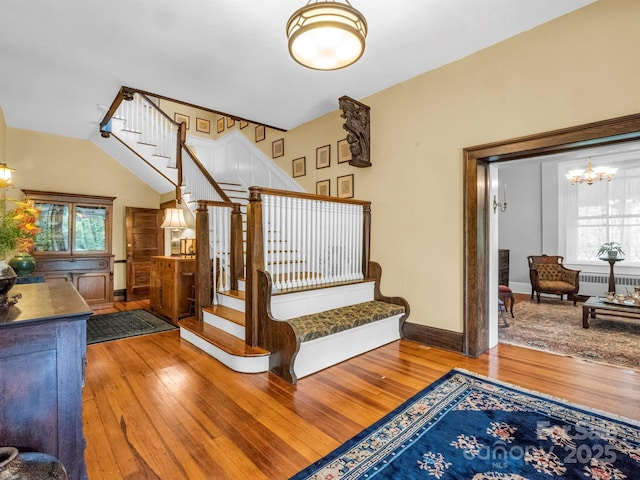 staircase featuring baseboards, radiator heating unit, an inviting chandelier, and hardwood / wood-style flooring