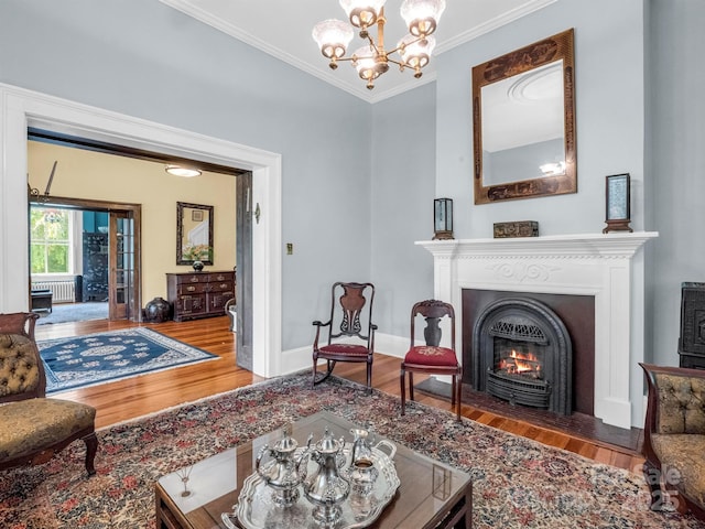 living room featuring crown molding, baseboards, a fireplace with flush hearth, wood finished floors, and a notable chandelier