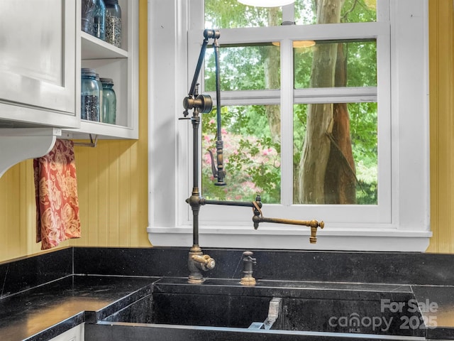 kitchen with dark countertops, wood walls, white cabinetry, and glass insert cabinets