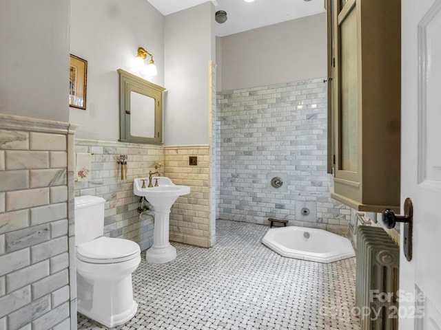 full bath featuring tiled bath, radiator, a wainscoted wall, toilet, and tile walls