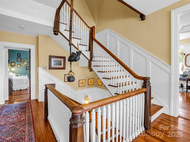 stairway with a decorative wall, wood-type flooring, and wainscoting