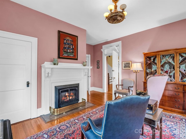 office area featuring a notable chandelier, a glass covered fireplace, baseboards, and wood finished floors