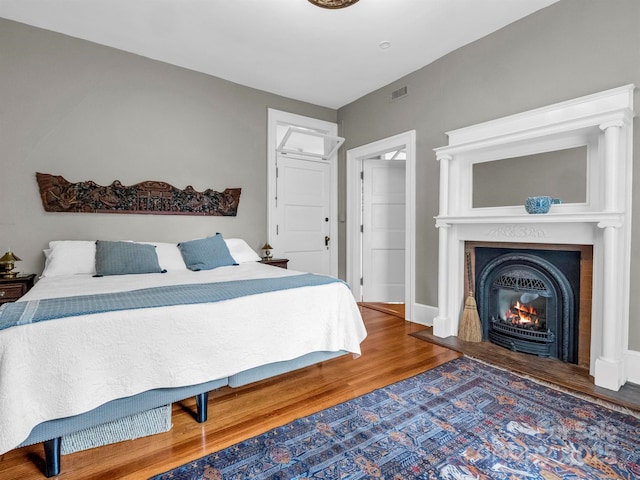 bedroom featuring a glass covered fireplace, visible vents, baseboards, and wood finished floors