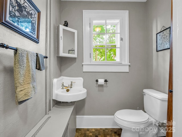 bathroom featuring toilet, baseboards, and a sink