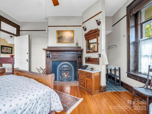 bedroom with baseboards, a glass covered fireplace, and light wood finished floors