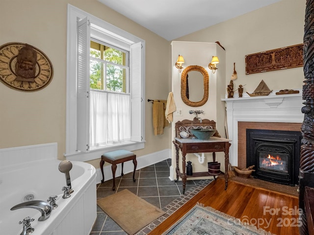 interior space featuring a bath, a glass covered fireplace, tile patterned flooring, and baseboards