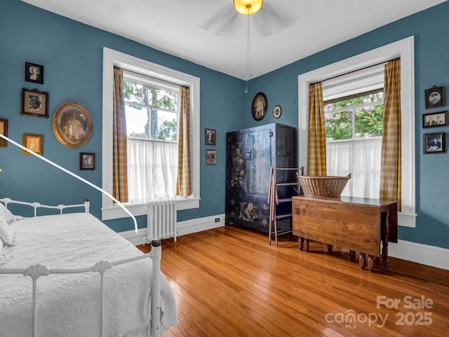 bedroom featuring hardwood / wood-style flooring, radiator, a ceiling fan, and baseboards