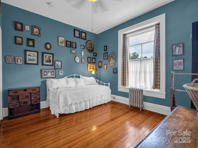 bedroom featuring radiator heating unit, baseboards, wood-type flooring, and ceiling fan