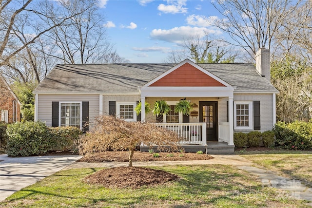 bungalow-style home with brick siding, a shingled roof, a chimney, covered porch, and a front yard