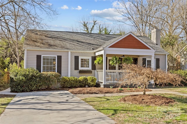 view of front of property with covered porch, a shingled roof, a chimney, and brick siding