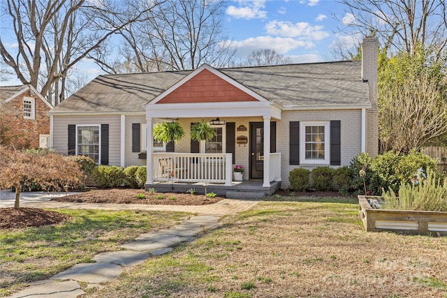 bungalow-style house with brick siding, a vegetable garden, a chimney, a porch, and a front yard