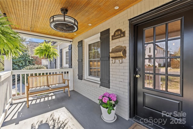 view of exterior entry with a porch and brick siding