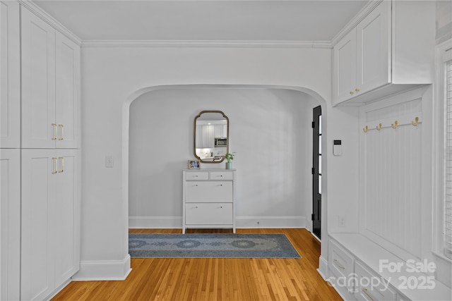 interior space with arched walkways, crown molding, light wood-style flooring, and baseboards