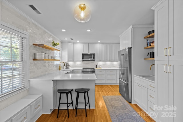 kitchen featuring open shelves, visible vents, appliances with stainless steel finishes, a sink, and a peninsula