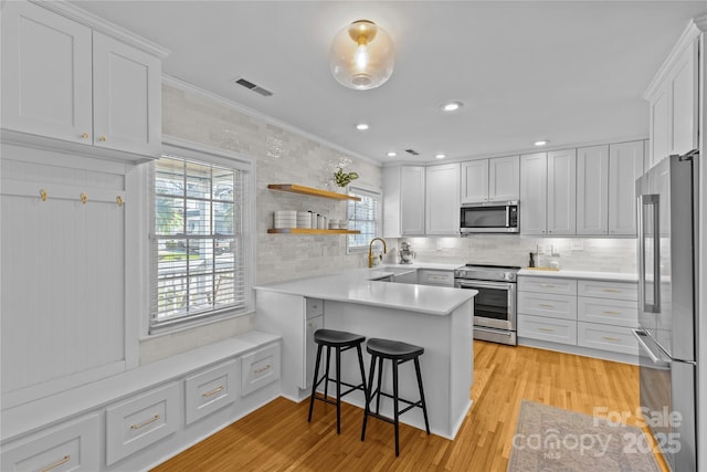 kitchen featuring light wood-style flooring, a peninsula, stainless steel appliances, crown molding, and a sink