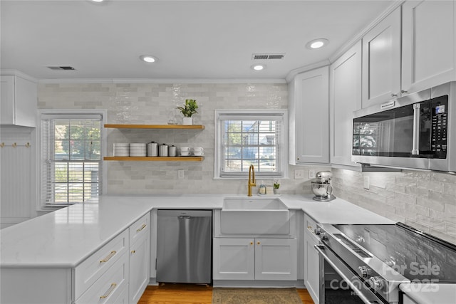 kitchen featuring stainless steel appliances, a peninsula, a sink, visible vents, and crown molding